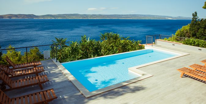Ein Privatpool über dem Meer, um ihn herum einige Holzliegen und Bäume