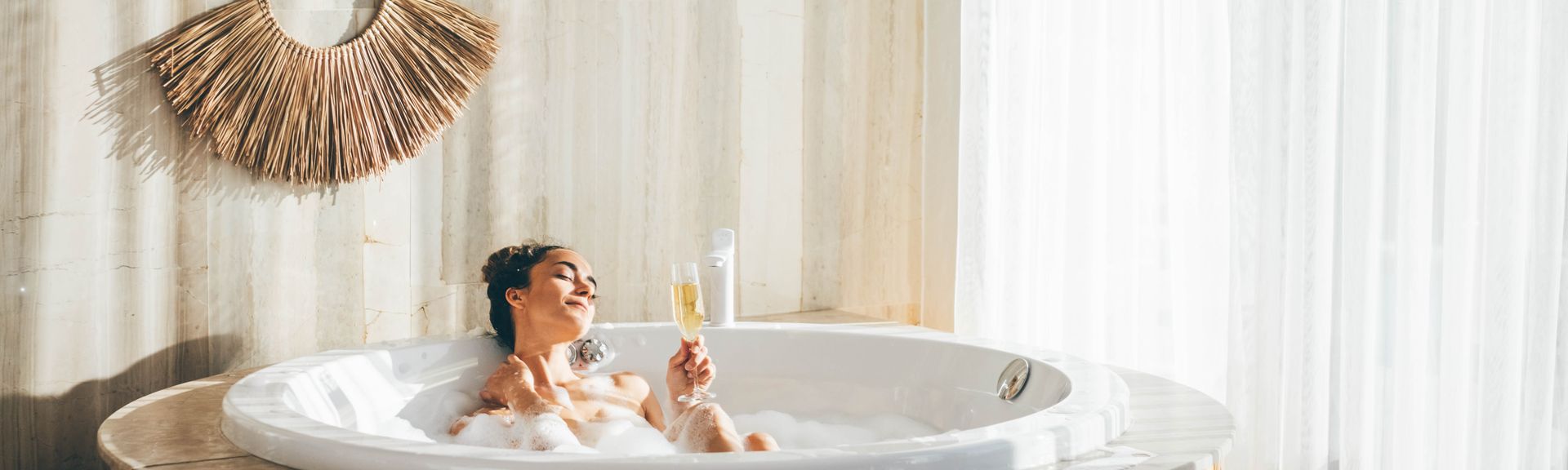 Eine Frau sitzt in einem Whirlpool in einem modernen Hotelzimmer und trinkt ein Glas Sekt