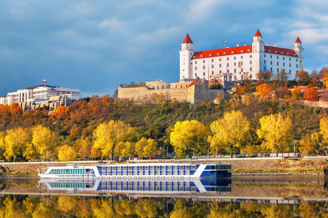 Flusskreuzfahrtschiff fährt an einer herbstlichen Landschaft mit einem weißen Schloss vorbei