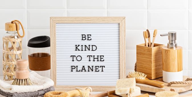 Eine Ablage vor einer Fliesenwand, Mehrere Handtücher, Bürsten und Seife, in der Mitte steht ein Schild mit der Aufschrift "BE KIND TO THE PLANET"
