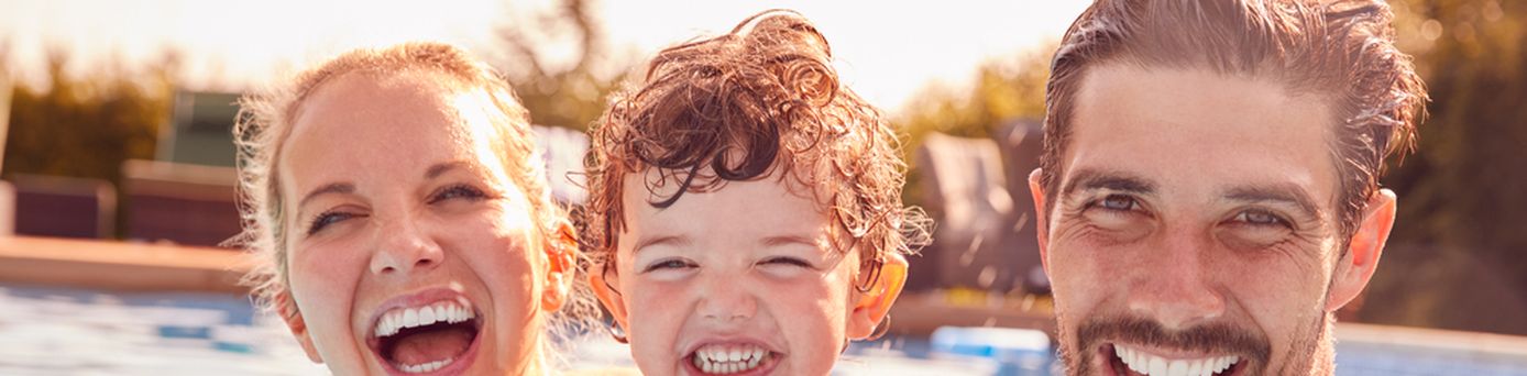 Eltern mit einem Kind spielen im Pool und lachen in die Kamera