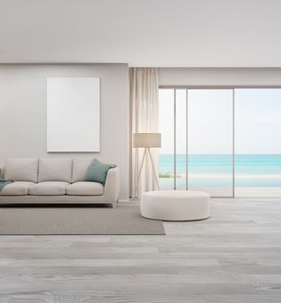 Blick auf das Sofa in einem Hotelzimmer. Rechts davon ist eine Glasfront mit offener Tür, die zu einem Pool führt. Das Meer ist im Hintergrund zu sehen