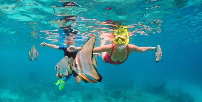 Zwei Kinder tauchen mit Taucherbrille und Schnorchel zwischen Fischen