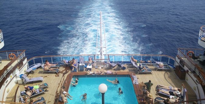 Im Pool am Heck eines Kreuzfahrtschiffes sieht man einige Urlauber schwimmen und sich sonnen