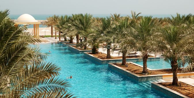 Poollandschaft mit Palmen und Blick auf das Meer