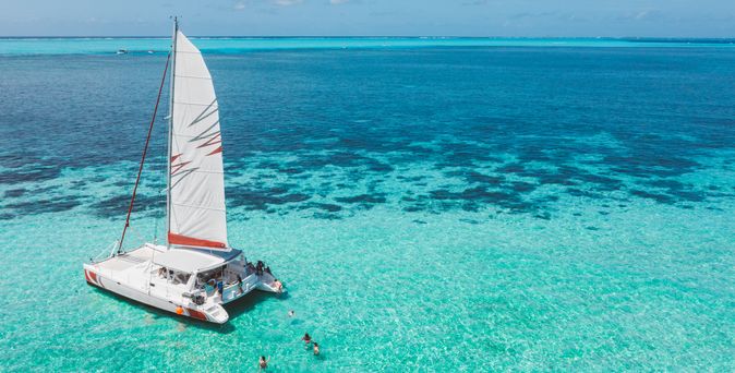 Ein Segelboot im Meer, dahinter schwimmen mehrere Personen