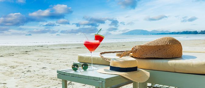 Eine Liege und ein Tisch mit einem Sonnenhut und einem Getränk am Strand