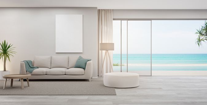 Blick auf das Sofa in einem Hotelzimmer. Rechts davon ist eine Glasfront mit offener Tür, die zu einem Pool führt. Das Meer ist im Hintergrund zu sehen