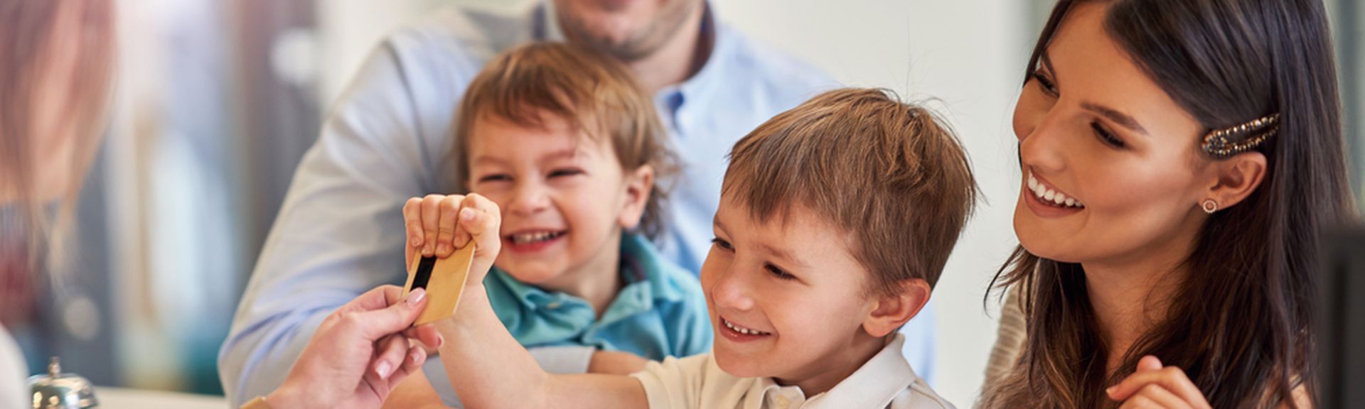 Eine Familie mit zwei Kindern beim Check-In in, Die Rezeptionistin reicht dem kleinen Kind die Zimmerkarte