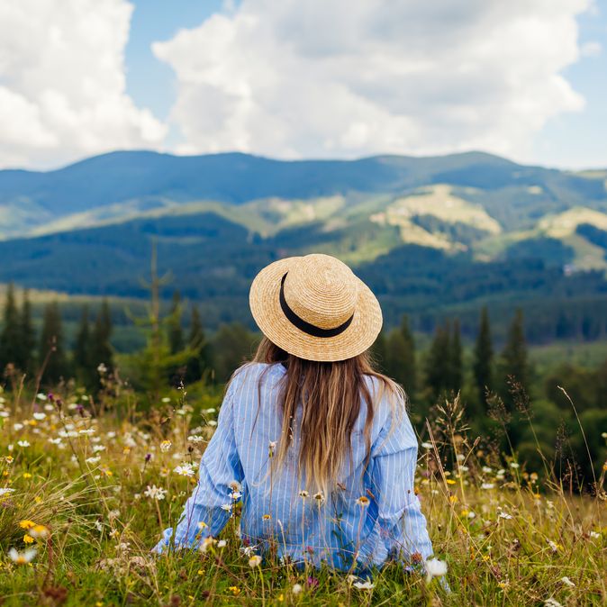Frau liegt im Gras umgeben von einer Berglandschaft