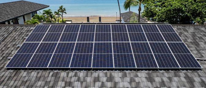 Ein Dach mit Solarplatten, im Hintergrund ein Strand und das Meer