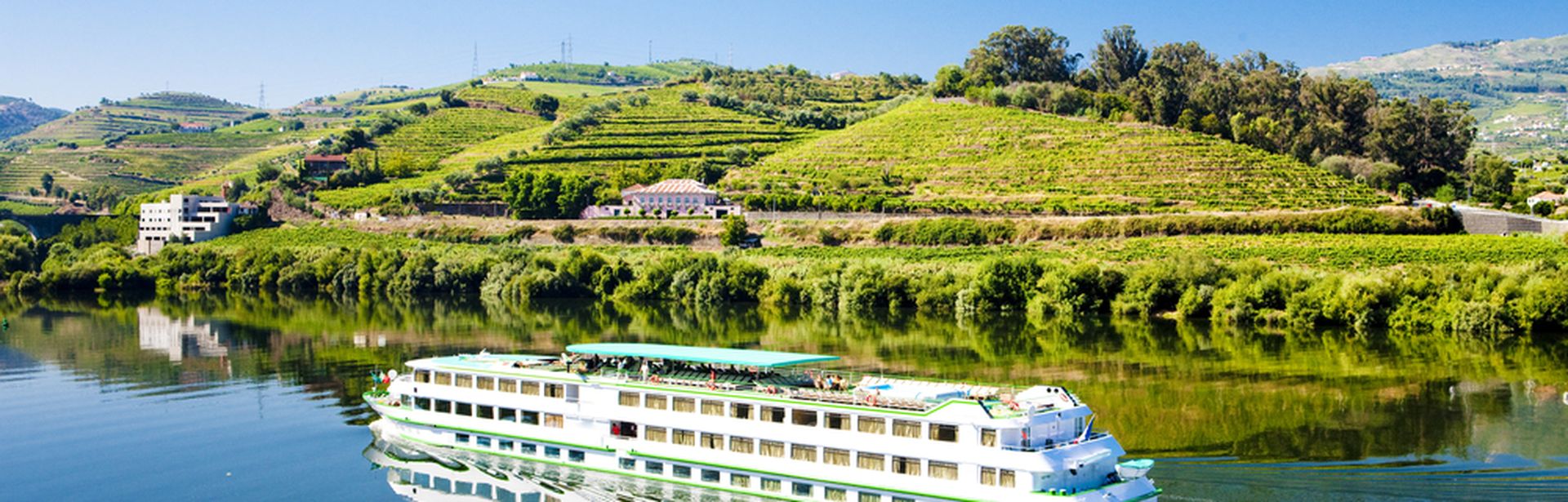 Flusskreuzfahrtschiff, dass durch eine hüglige, grüne Landschaft fährt
