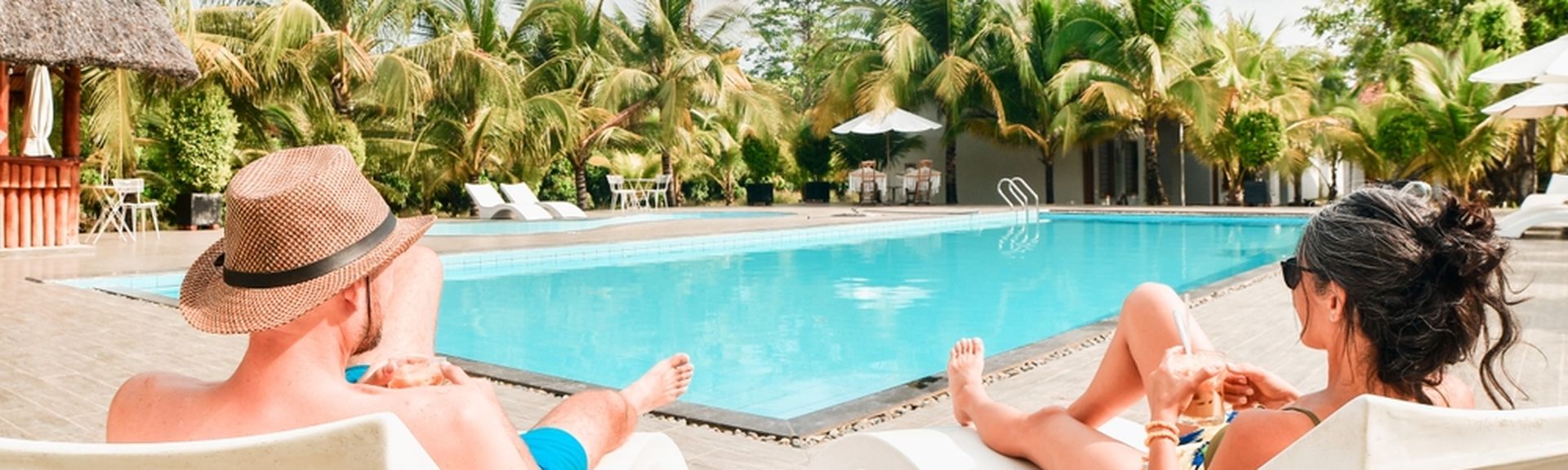 Eine Frau und ein Mann liegen auf weißen Liegen am Pool und trinken jeweils ein Getränk