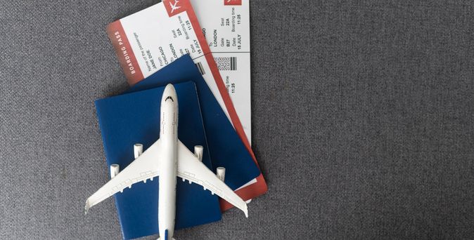 Ein Miniaturflugzeug liegt auf einem Reisepass in dem sich zwei Flugtickets befinden