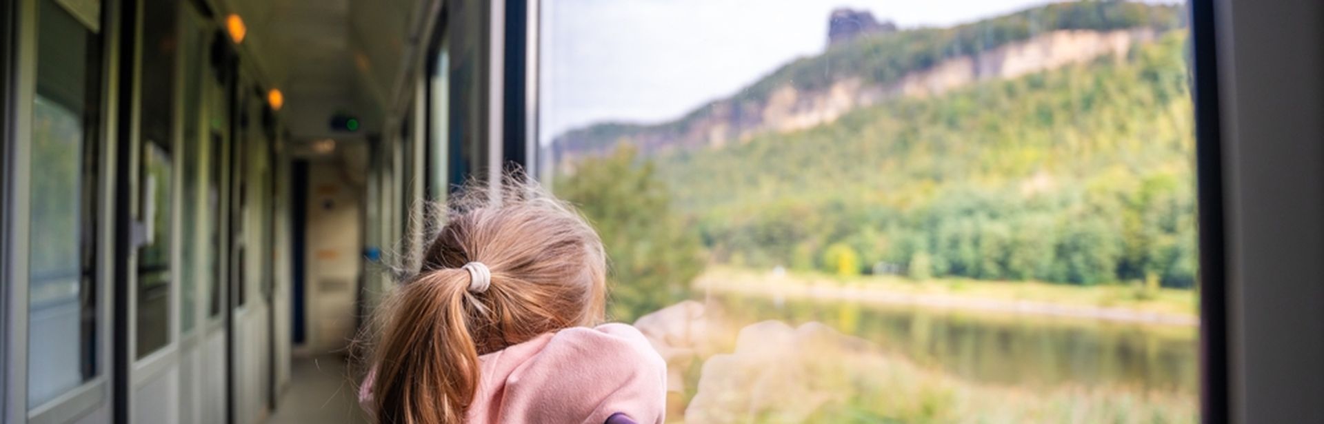 Ein Kind steht am Fenster in einem Zug und schaut auf die grüne Landschaft