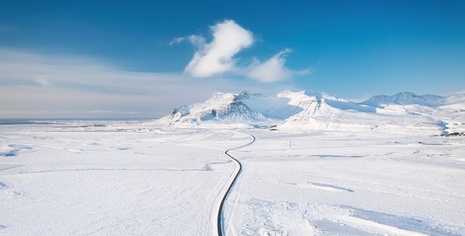 Weg durch eine flache Schneelandschaft mit Bergen im Hintergrund