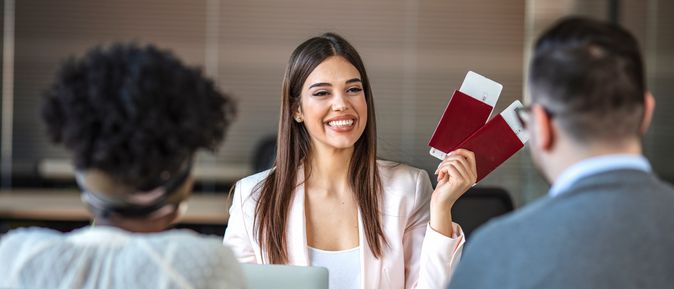 Eine lächelnde Reiseberaterin hält Ihren Kunden zwei Reisepässe mit Flugtickets hin