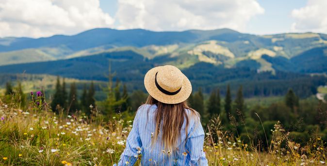 Frau liegt im Gras umgeben von einer Berglandschaft