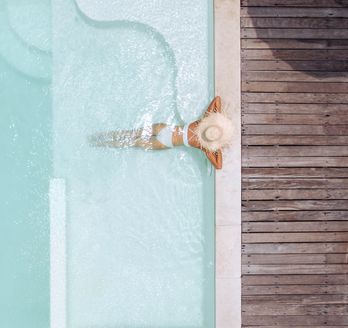 Eine Frau mit weißem Sonnenhut lehnt am Rand eines eleganten Pools