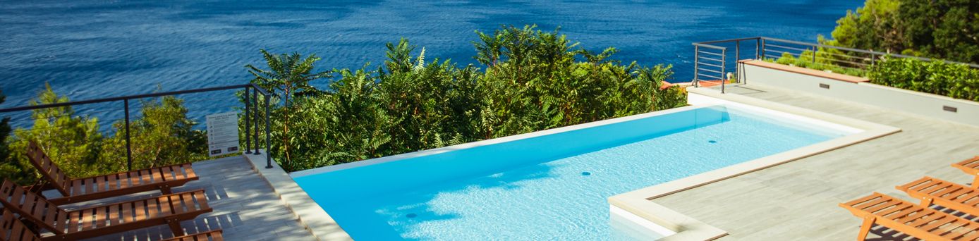 Ein Privatpool über dem Meer, um ihn herum einige Holzliegen und Bäume