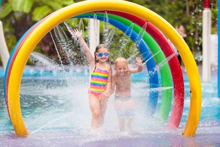 Zwei Kinder laufen durch bunte Bögen aus denen Wasser auf sie gespritzt wird