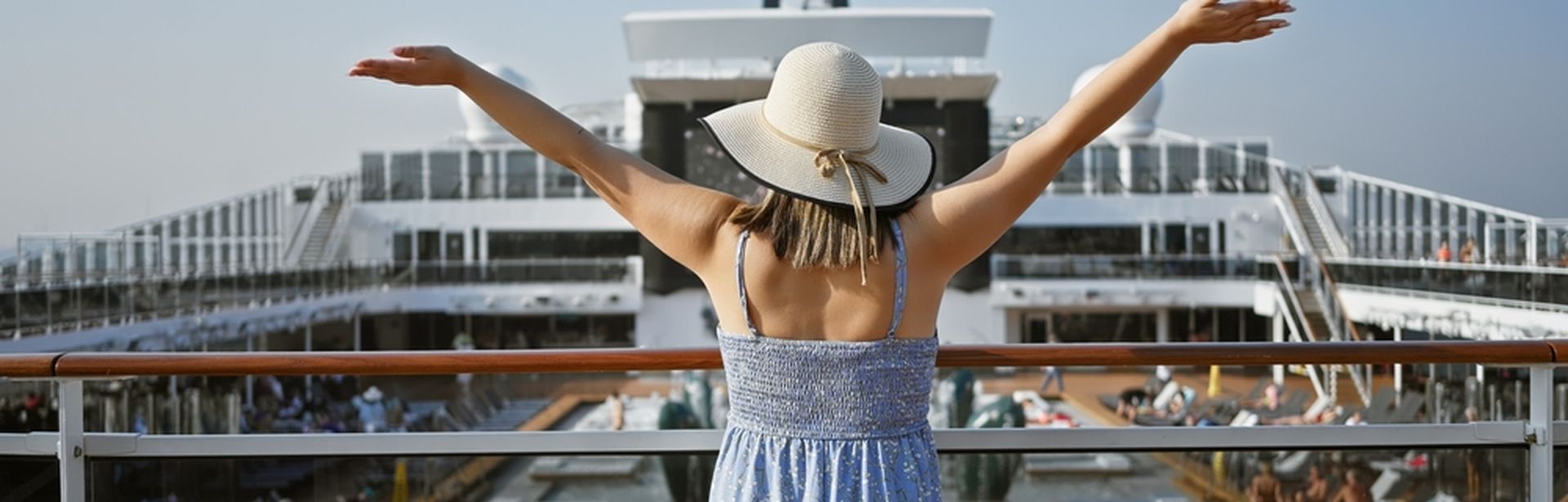Eine Frau steht auf dem Pooldeck eines Kreuzfahrtschiffes und streckt die Arme in die Luft