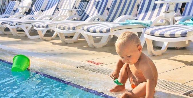 Ein Kleinkind sitzt am Rand eines Pools und spielt mit einer Spielzeugschaufel