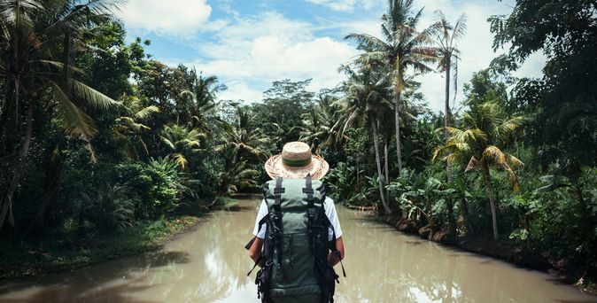 Frau mit Strohhut und Rucksack schaut auf Wasser und Palmen