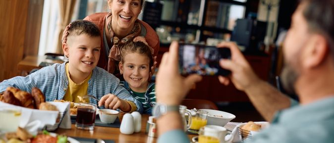 Zwei Kinder und eine Frau werden von einem Mann am Frühstückstisch fotografiert
