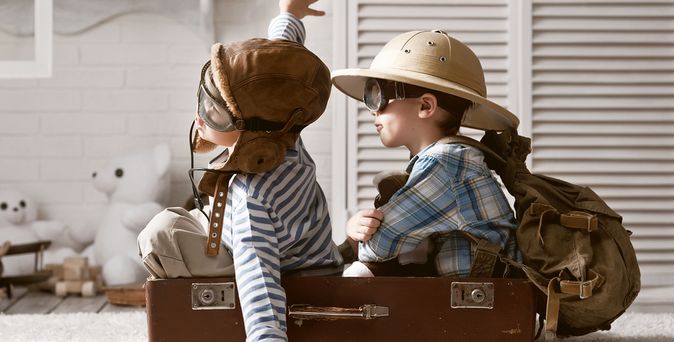 Zwei Jungs mit Fliegerhelmen sitzen in einem braunen Koffer und spielen Flugzeug