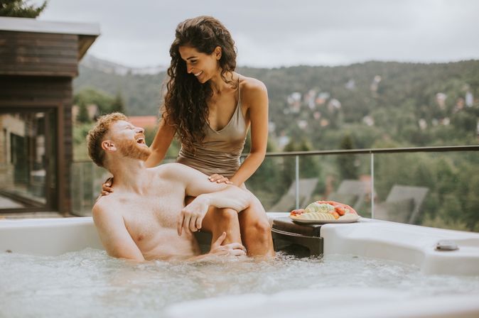 Ein Mann sitzt im Whirlpool und eine Frau sitzt hinter ihm auf dem Rand des Whirlpools