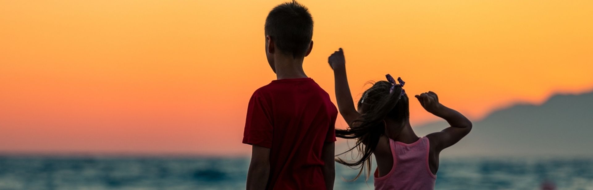 Zwei Kinder schauen bei Sonnenuntergang aufs Meer