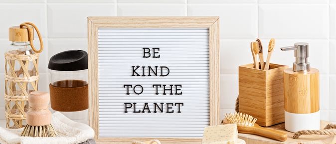 Eine Ablage vor einer Fliesenwand, Mehrere Handtücher, Bürsten und Seife, in der Mitte steht ein Schild mit der Aufschrift "BE KIND TO THE PLANET2