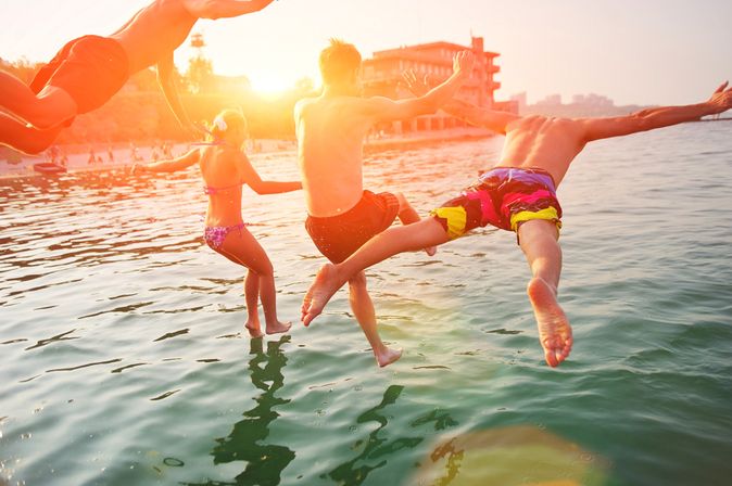 Vier Personen springen bei Sonnenuntergang ins Meer