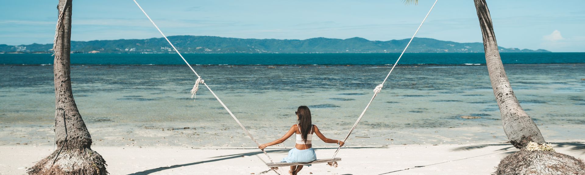 Frau auf einer Schaukel zwischen zwei Palmen am Meer