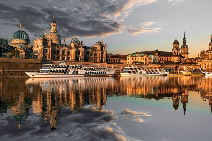 Flusskreuzfahrschiffe fahren an alten Bauwerken vorbei, die sich im stillen Wasser des Flusses spiegeln