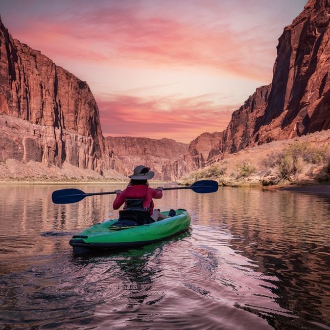Eine Person sitzt in einem Grünen Kanu und schaut auf einen pinken Sonnenauf/untergang
