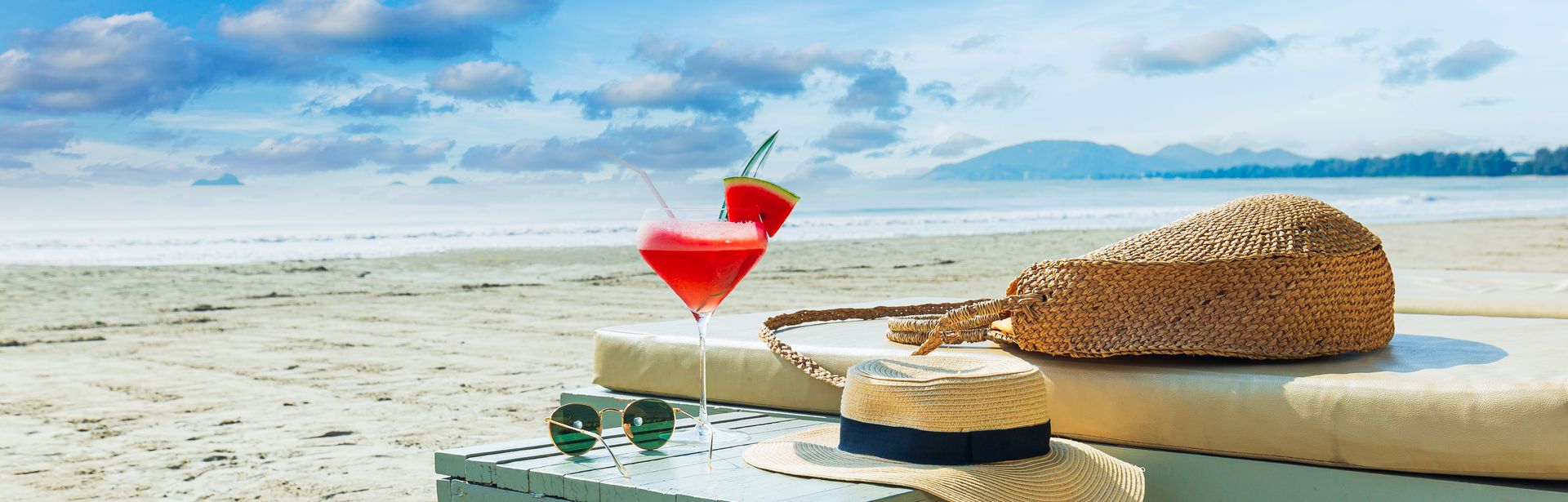 Eine Liege und ein Tisch mit einem Sonnenhut und einem Getränk am Strand