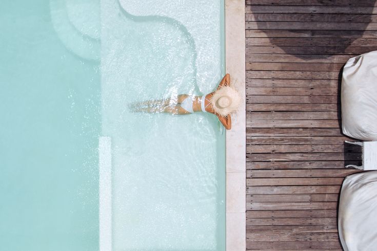 Eine Frau mit weißem Sonnenhut lehnt am Rand eines eleganten Pools