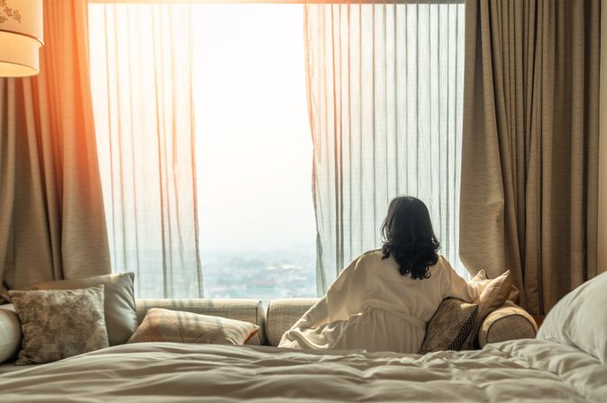 Frau sitzt in Ihrem Hotelzimmer auf dem Sofa und schaut aus dem Fenster