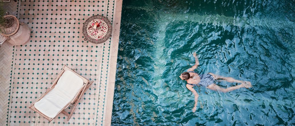 Frau schwimmt in einem Pool; Neben dem Pool, auf der Terrasse steht eine Liege