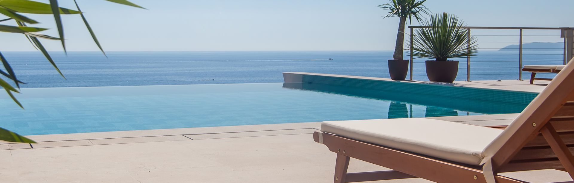 Eine Liege und an einem Infinity Pool, im Hintergrund das Meer