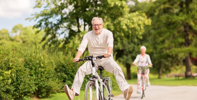Zwei Rentner auf dem Fahrrad, der Mann im Vordergrund lacht und streckt seine Beine weg