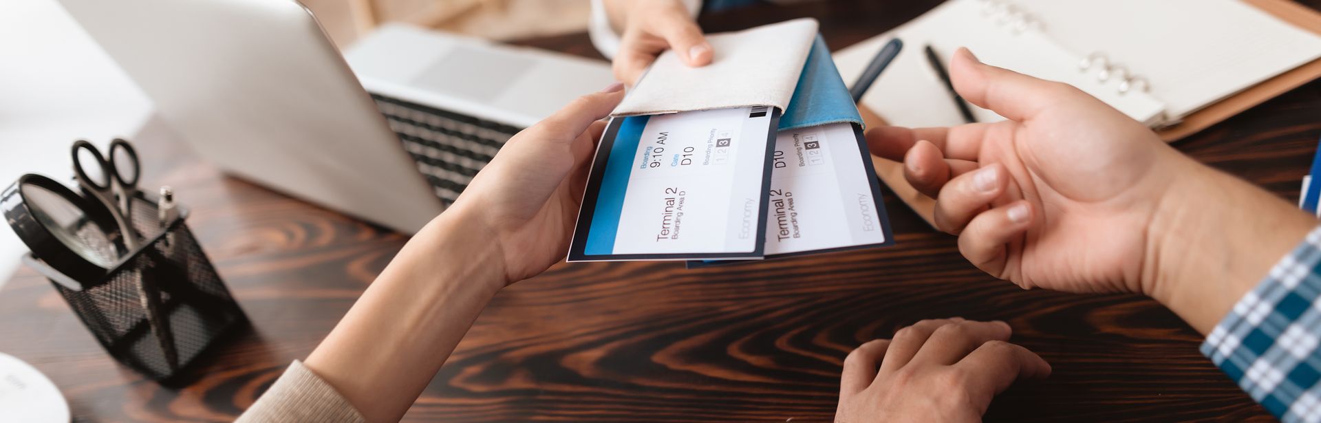 Eine Frau sitzt am Schreibtisch und übergibt zwei Personen Ihre Flugtickets