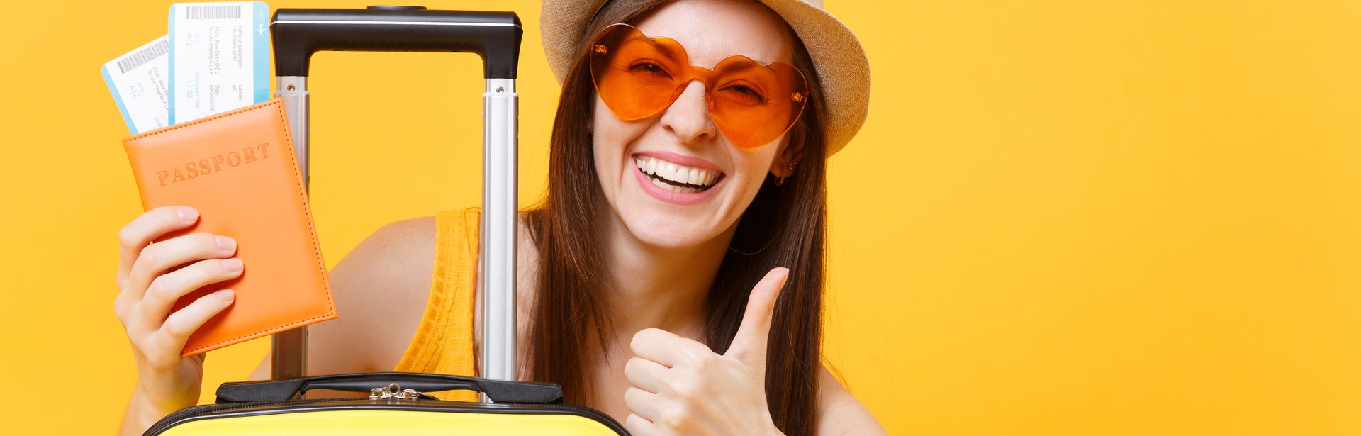 Frau vor gelbem Hintergrund, die hinter einen Koffer hervor schaut und einen Reisepass mit Flugtickets in einer Hand hält. Die Frau zeigt einen Daumen nach oben mit der anderen Hand