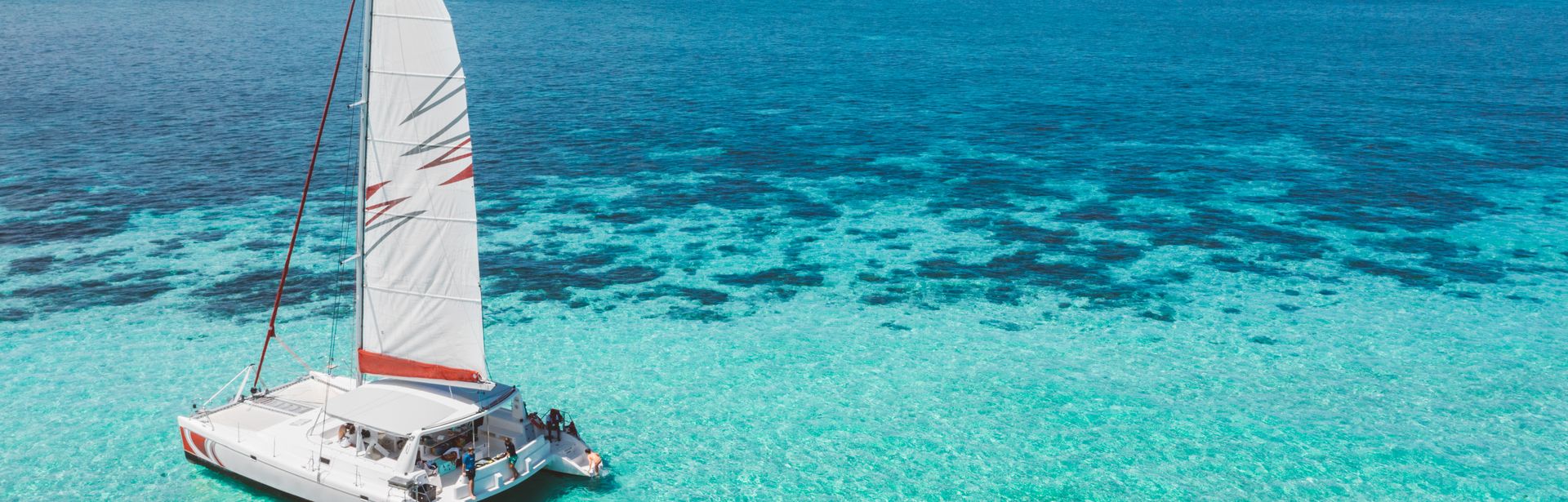 Ein Segelboot im Meer, dahinter schwimmen mehrere Personen