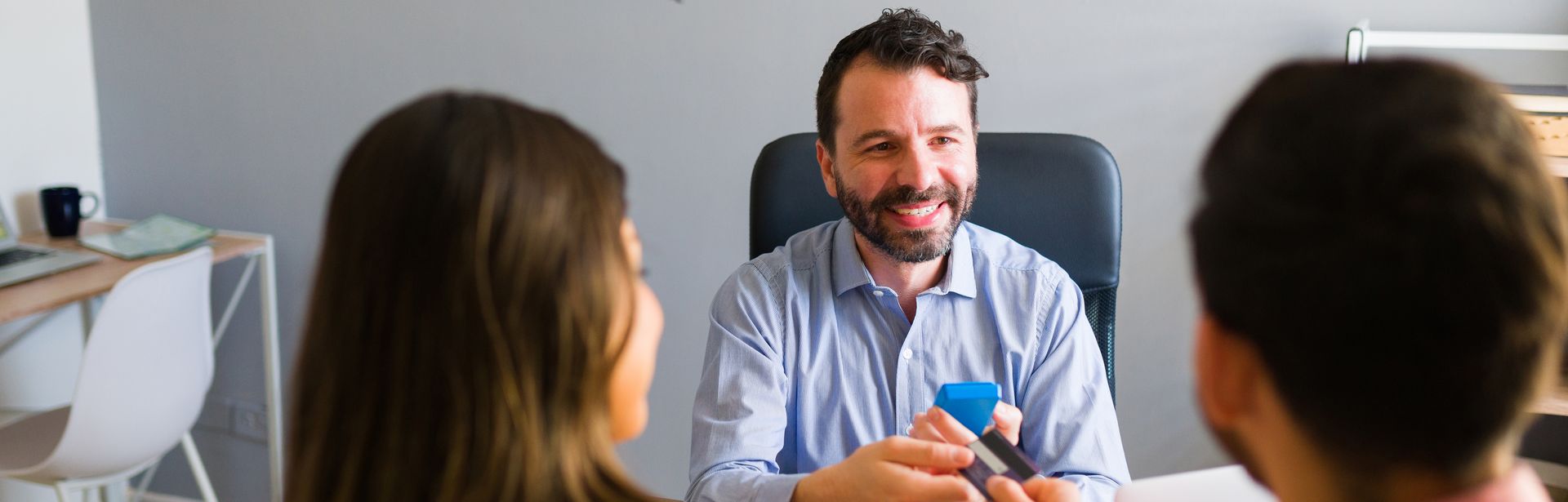 Ein Paar sitzt mit einem Reiseberater am Schreibtisch und gibt Ihm eine Kreditkarte