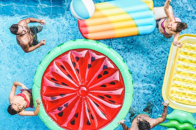 Ein Pool von oben, mehrere Personen und Pool Floaties in Frucht Formen