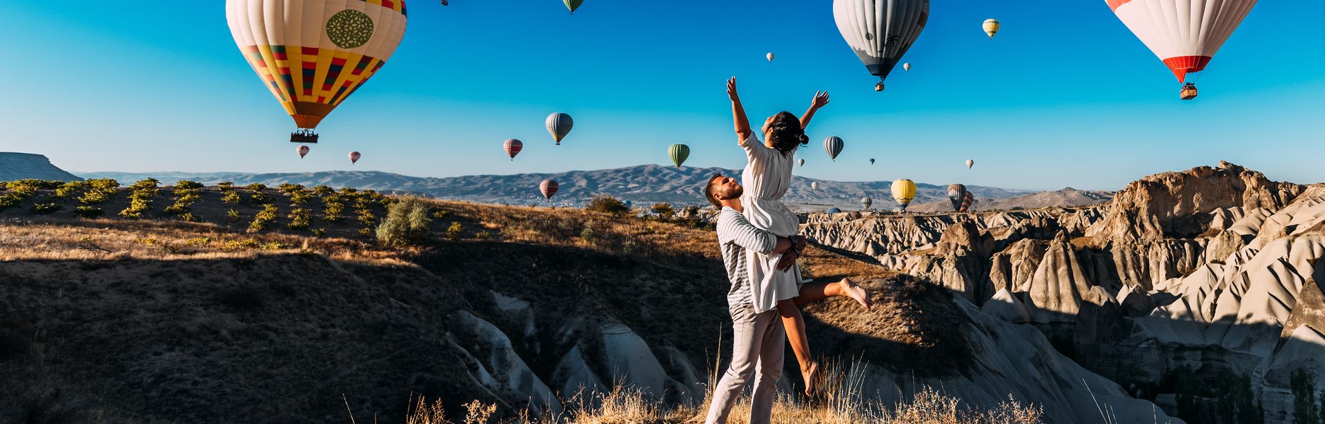 Ein Mann trägt eine Frau im Arm, um Sie herum schweben Heißluftballons durch die Luft