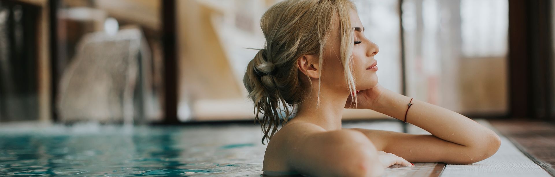 Frau lehnt am Rand eines indoor Pools und hat die Augen geschlossen